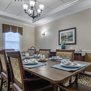 A neatly arranged dining room with a wooden table set for four, featuring a chandelier and elegant decor.