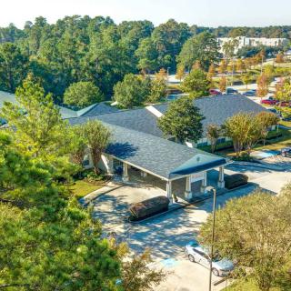 Aerial view of a building surrounded by trees and a parking lot in a suburban area.