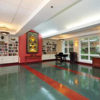 A spacious hallway with a piano, large artwork on the wall, and ample natural light from multiple windows.