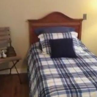 A cozy bedroom featuring a single bed with plaid bedding and a nightstand with a lamp.