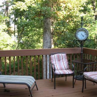 A cozy outdoor deck with chairs and a lounge chair surrounded by lush trees.