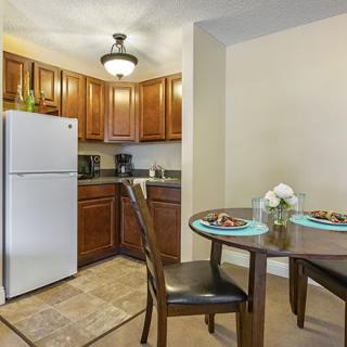 A cozy kitchen and dining area featuring wooden cabinets, a refrigerator, and a small dining table set for two with decorative flowers.