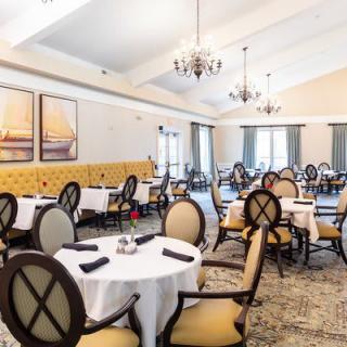 An elegant dining room with neatly arranged tables and chairs, adorned by chandeliers.