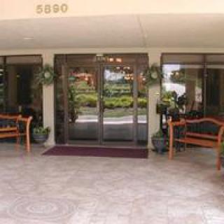 A building entrance with glass doors, flanked by benches and potted plants.