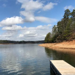 A peaceful lake view with a dock extending into the water, surrounded by trees and under a partly cloudy sky.