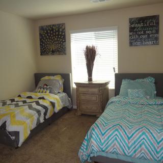 A cozy bedroom featuring two twin beds with colorful bedding, a nightstand with a decorative item, and wall art above each bed.