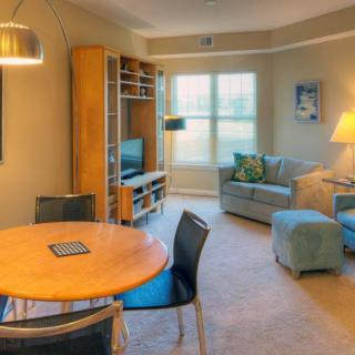 A cozy living room with a dining area featuring a round table, chairs, a comfortable sofa set, and a television stand near a large window.