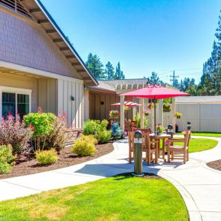 A sunny patio area with outdoor furniture and an umbrella, surrounded by a well-maintained garden and landscaping.