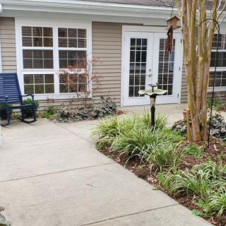 A cozy patio area with a pathway surrounded by lush garden plants and outdoor seating.