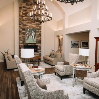A modern living room with high ceilings, featuring a central fireplace, elegant chandelier, and neutral-toned furnishings.