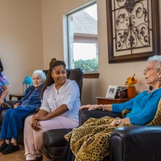 A group of seniors and a caregiver enjoying a conversation in a cozy living room.