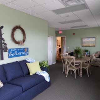 A cozy living room featuring a navy sofa, a wooden dining table with chairs, decorative wall art, and various plants creating an inviting atmosphere.