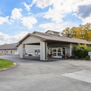 A hotel building with a covered entrance and surrounding landscape under a partly cloudy sky.