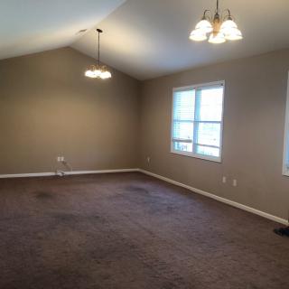 An empty living room with carpet flooring, neutral colored walls, and ceiling light fixtures.