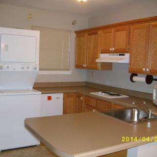 A kitchen with wooden cabinets, stacked washer and dryer, and a countertop with a sink.