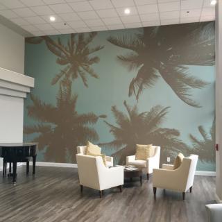 A modern lobby featuring a palm tree wall mural and a cozy seating area with chairs and a coffee table.