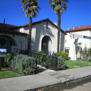 A sunny day view of a building with arched windows and palm trees lining the sidewalk.