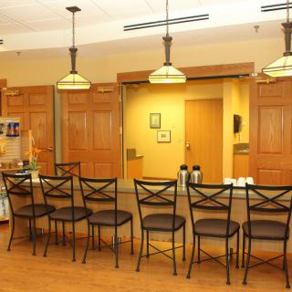 A well-lit kitchen area with a row of bar stools and pendant lighting above the countertop.