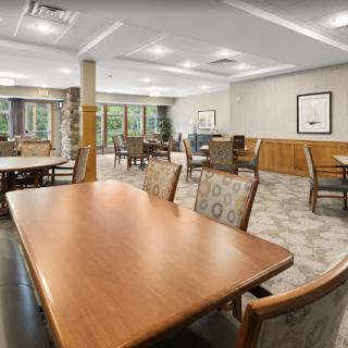 A spacious dining area with multiple tables and chairs, featuring natural lighting from large windows.