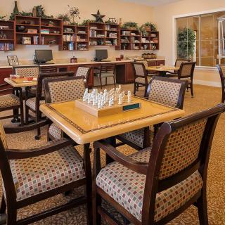 A cozy library with seating areas, bookshelves, and a chess set on the table.