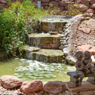 A serene garden with a cascading waterfall and a small pond, adorned with a statue of children sitting on a bench.