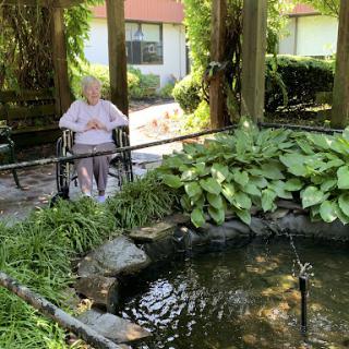 A serene moment in the garden, where an elderly woman enjoys the tranquility by a pond.