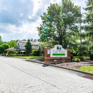 A suburban neighborhood street with houses and a welcoming sign surrounded by lush greenery.
