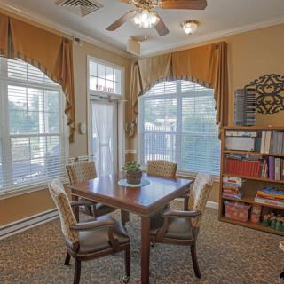 Cozy dining area with large windows and elegant curtains, featuring a wooden table and chairs alongside a well-stocked bookshelf.
