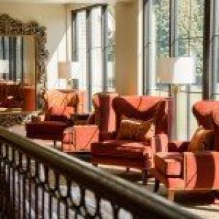 A stylish lounge area with red armchairs, large windows, and a decorative mirror.