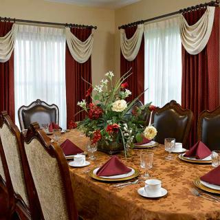 A formal dining room with an elegantly set table, complete with floral centerpiece and rich drapery.