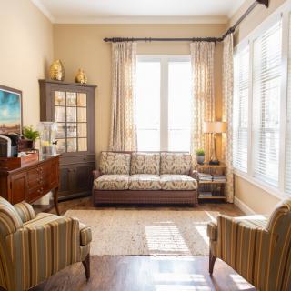 A cozy living room with a sofa, two armchairs, and natural light streaming through large windows.