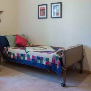 A neatly made bed with a colorful quilt and pillows, in a room with framed pictures on the wall.