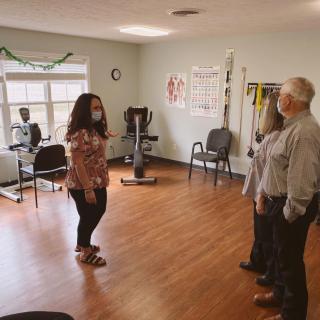 A small group of people wearing masks are having a discussion in an office with exercise equipment.