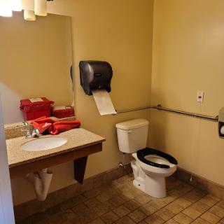 A view of a simple bathroom featuring a toilet, sink, mirror, and hand dryer with red towels.