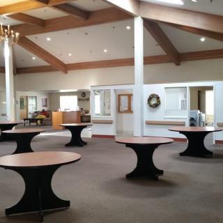A spacious banquet hall with round tables and wooden beam ceiling.