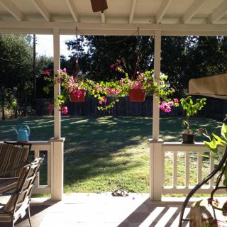 A sunny porch with outdoor furniture overlooking a backyard garden adorned with hanging plants.