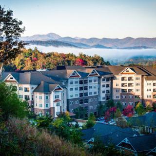 A scenic view of a residential building nestled in a mountainous landscape with fog and colorful trees.