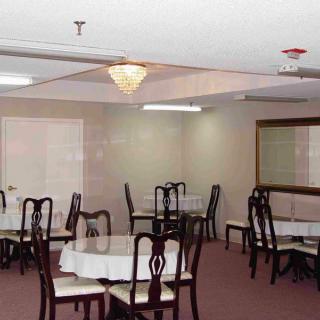 An empty dining room with round tables covered in white tablecloths and wooden chairs, illuminated by a chandelier.