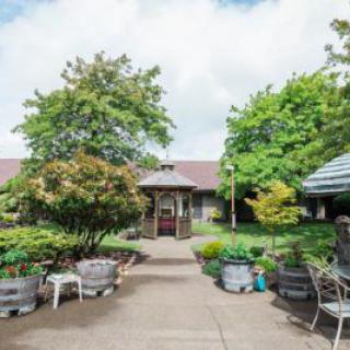 A peaceful garden area with a pathway leading to a gazebo, surrounded by lush greenery and outdoor seating.