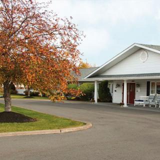 A white building with a covered entrance sits beside a tree displaying autumn foliage, under a cloudy sky.