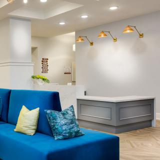 A modern lobby area featuring a blue sofa, decorative pillows, and a reception desk with stylish wall lighting.