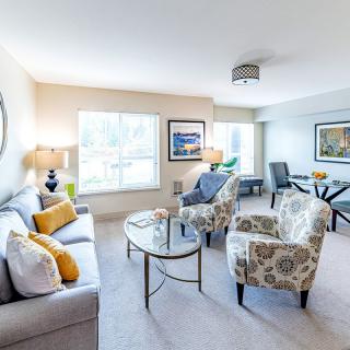 A bright, modern living room featuring a sofa, armchairs, and a glass coffee table, complemented by artwork and decorative elements.