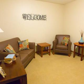 A cozy living room with a sofa and armchair, accented by colorful pillows and a 'WELCOME' sign on the wall.