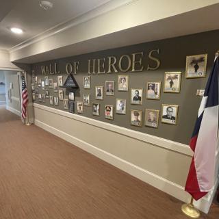 A hallway display titled 'Wall of Heroes' featuring photographs and memorabilia in tribute to military service members, accompanied by American and Texas flags.