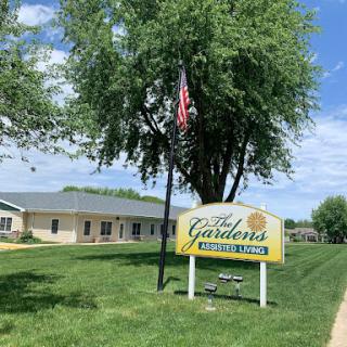 A peaceful community setting featuring a sign for a local establishment, surrounded by greenery and under a clear blue sky.