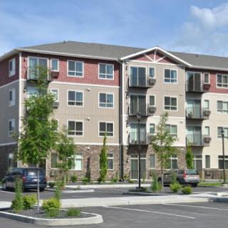 A modern apartment building surrounded by greenery and a parking area.