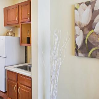 A small kitchen with wooden cabinets, a white refrigerator, and a decorative painting on the wall.