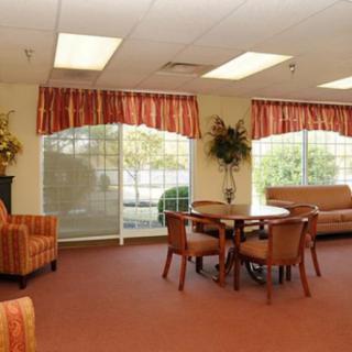 A cozy waiting room with chairs, a sofa, and a table, featuring large windows with red curtains.