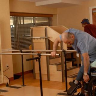 An elderly man engaging in physical therapy exercises with assistance in a healthcare facility.