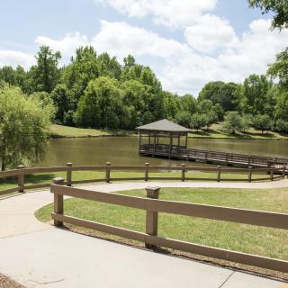A tranquil park scene with a gazebo by the lake, surrounded by lush trees and a curving walking path.
